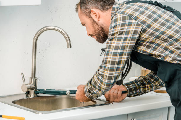 istock handsome plumber repairing tap with monkey wrench in kitchen 1049768982