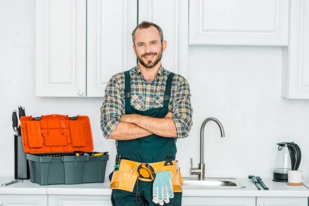 sonriendo apuesto fontanero de pie con los brazos cruzados y mirando a cámara en la cocina - adjustable wrench fotos fotografías e imágenes de stock