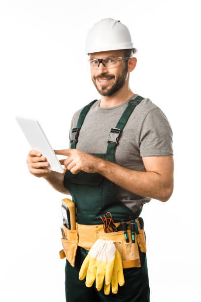 istock smiling handsome electrician in helmet and protective glasses using tablet isolated on white 1049769204