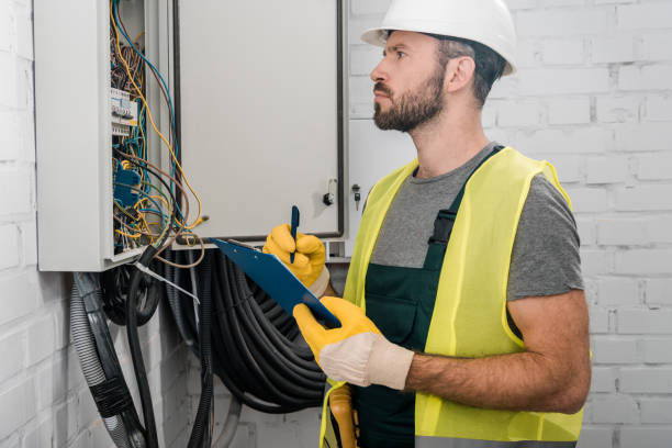 side view of serious electrician holding clipboard and checking electrical box in corridor