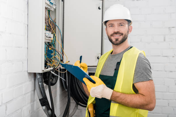 istock smiling handsome electrician holding clipboard near electrical box in corridor and looking at camera 1049771102