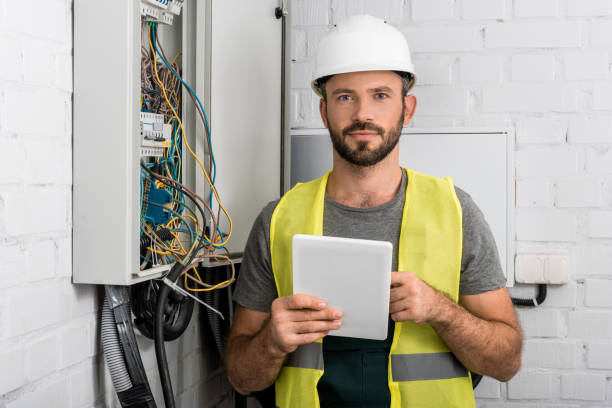 istock handsome electrician holding tablet near electrical box in corridor and looking at camera 1049771390