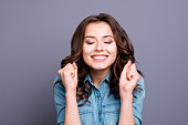 Trendy sweet tender magnificent nice cheerful adorable lovely attractive stylish brunette girl with wavy hair in casual denim shirt, showing luck gesture, closed eyes, isolated over grey background