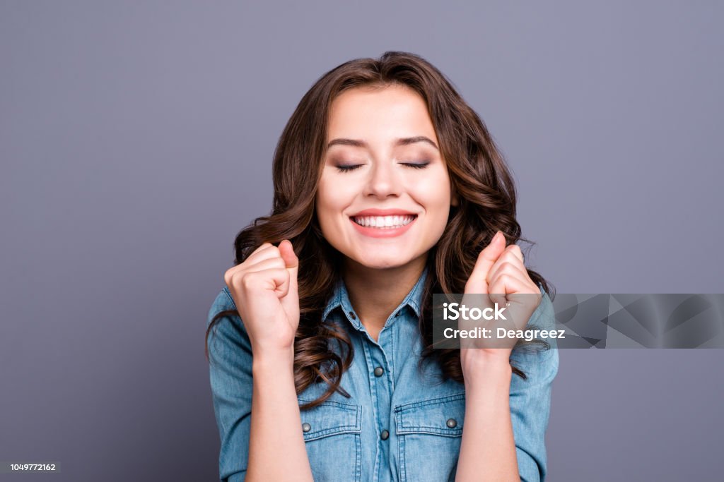 Trendy sweet tender magnificent nice cheerful adorable lovely attractive stylish brunette girl with wavy hair in casual denim shirt, showing luck gesture, closed eyes, isolated over grey background Women Stock Photo