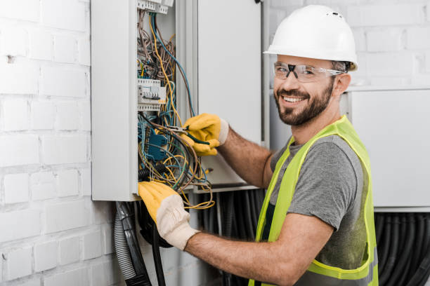 smiling handsome electrician repairing electrical box with pliers in corridor and looking at camera stock photo