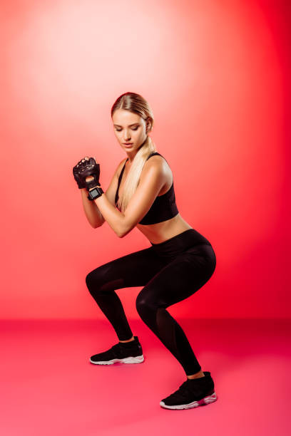 istock attractive sportswoman training and doing squats on red 1049781224