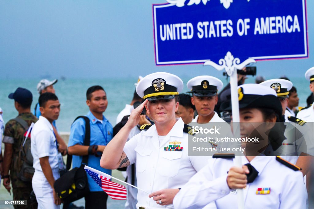 Greeting US navy officer with small US flag Greeting US navy officer with small US flag in group of navy officers walking in asean fleet parade in Pattaya. In background are journalists and photographers. A woman is carrying sig with letters UNITED STATES OF AMERICA. Asia Stock Photo