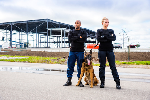A male and female K-9 security professionals with a Belgian Malinois outside a building under construction.
