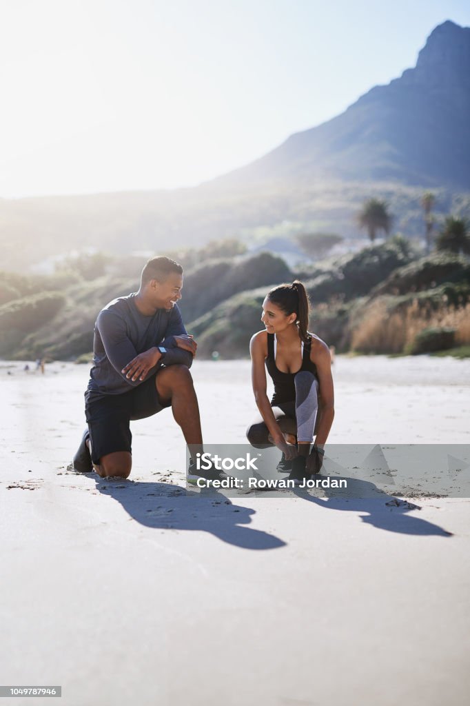Starting their day out in the fresh air with some fitness Shot of a sporty young couple tying their shoelaces while out for a run along the beach Shoe Stock Photo