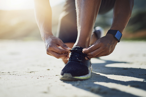 Closeup shot of an unrecognizable man tying his shoelaces while exercising outdoors