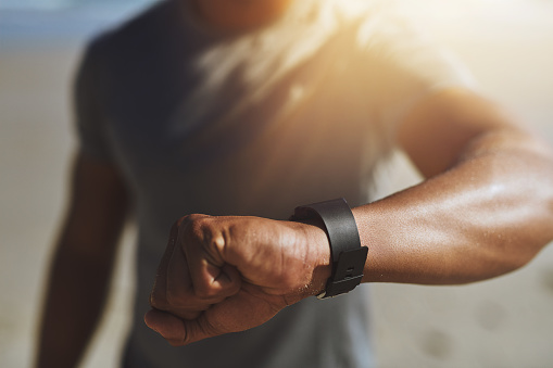 Closeup shot of an unrecognizable man checking his smartwatch while exercising outdoors