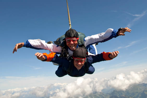 os para-quedistas em tandem mergulham através de sublimes céus acima de montanhas - skydiving parachute parachuting taking the plunge - fotografias e filmes do acervo
