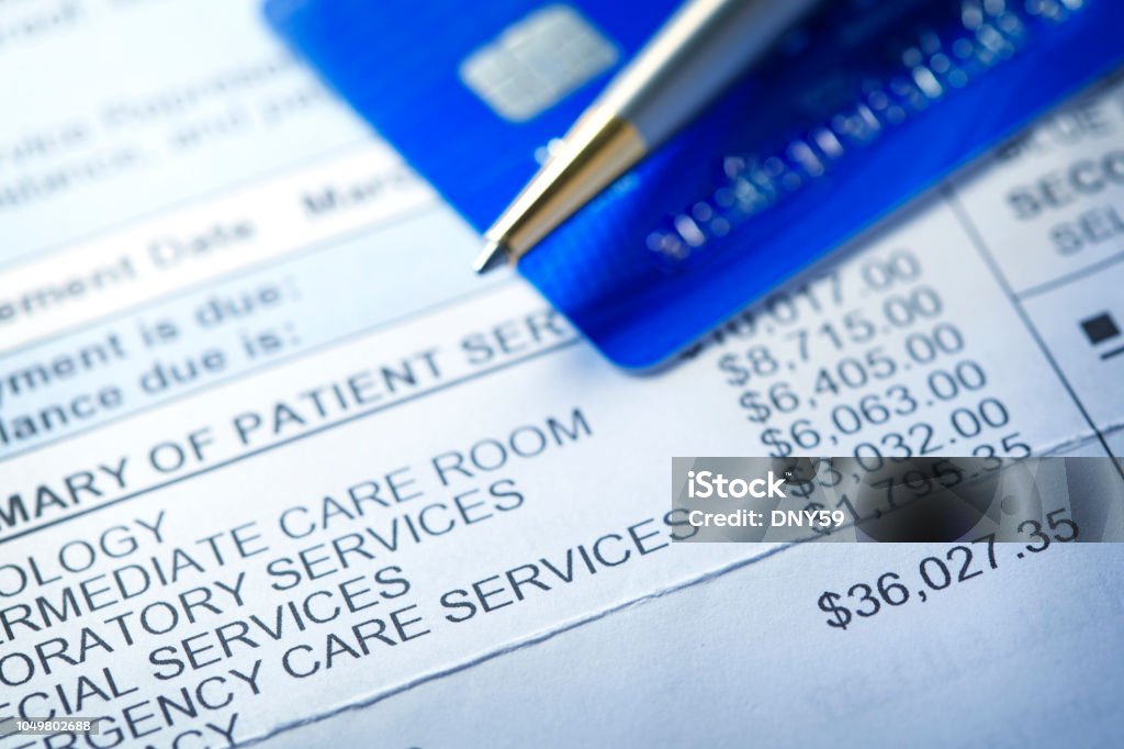 Credit Card On A Hospital Invoice A hospital bill for $36,000 with a line item of various charges is photographed with a very shallow depth of field. A credit card and a ballpoint pen rest out of focus in the background. Healthcare And Medicine Stock Photo