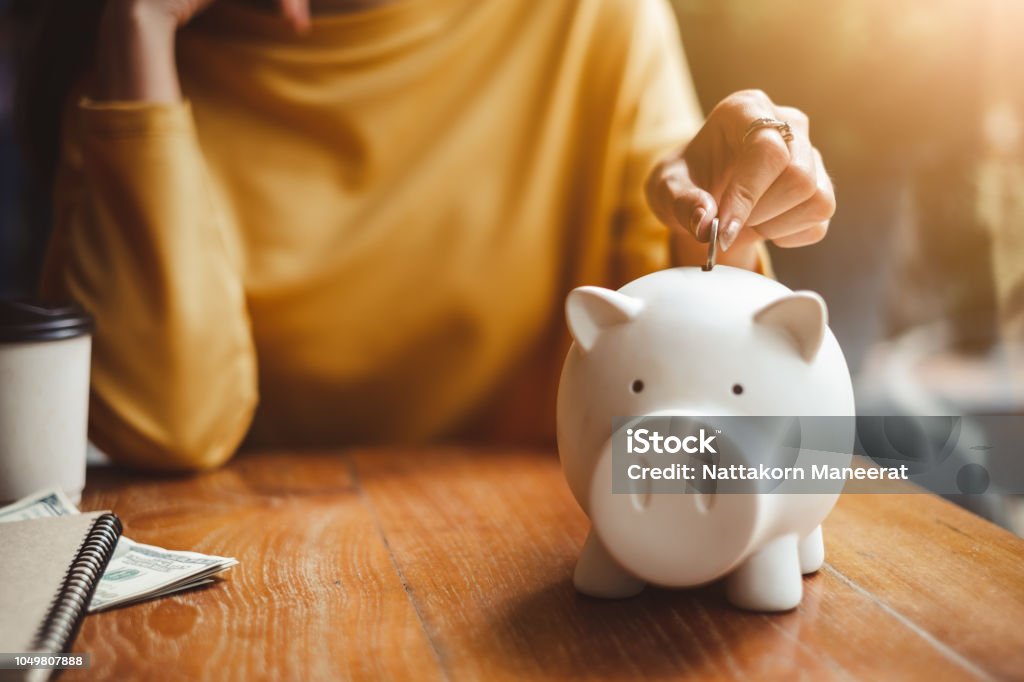 woman hand putting money coin into piggy for saving money wealth and financial concept. Savings Stock Photo