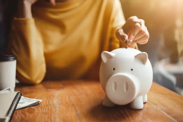 Photo of woman hand putting money coin into piggy for saving money wealth and financial concept.