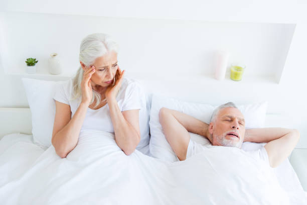 relajarse, descansar, jubilado, concepto. ¡estoy muy cansado! mujer de pelo gris mira a un lado, orejas de titular y cerca ojos emplazamiento en la ropa de cama, sábanas y mirada en soñar a marido dormido - couple love snoring sleeping fotografías e imágenes de stock