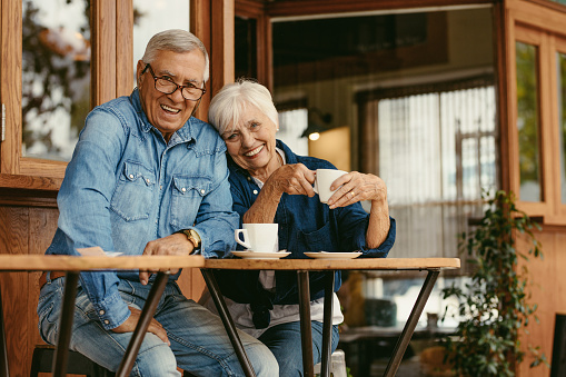 Senior couple in love at coffee shop. Beautiful portrait of old man and woman sitting at cafe table with coffee looking at camera.