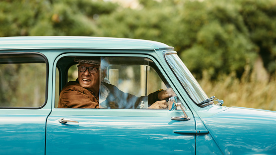 Senior man driving a classic car. Old man looks out of the window of his car before making a turn on road.