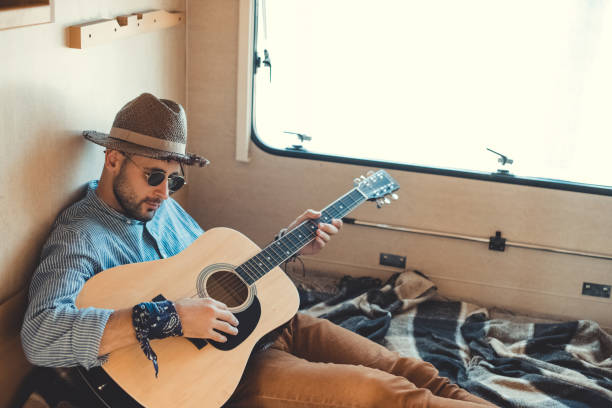 istock handsome man in hat playing guitar inside of campervan 1049819056
