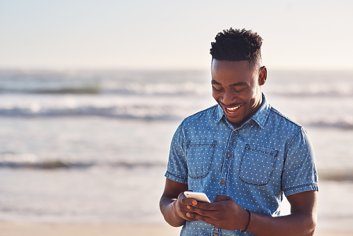 Shot of a happy young man using a mobile phone at the beach