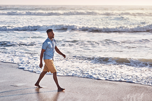 Shot of a handsome young man going for a walk along the beach