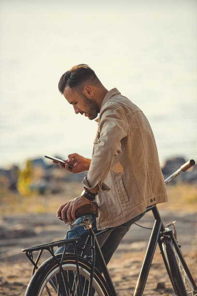 istock young handsome man using smartphone and leaning on bicycle outdoors 1049840588
