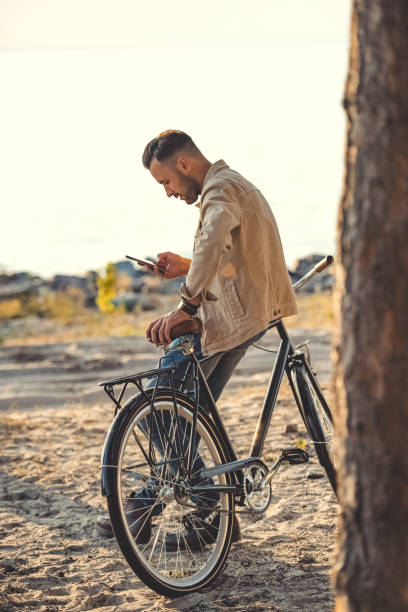 istock young man using gadget and leaning on bicycle near sea 1049840628