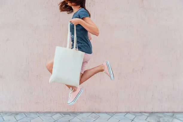 Young woman is jumping with white cotton bag in her hands. Mock up.