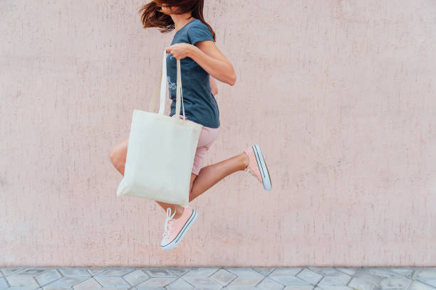 young woman is jumping with white cotton bag in her hands. - recycled bag imagens e fotografias de stock