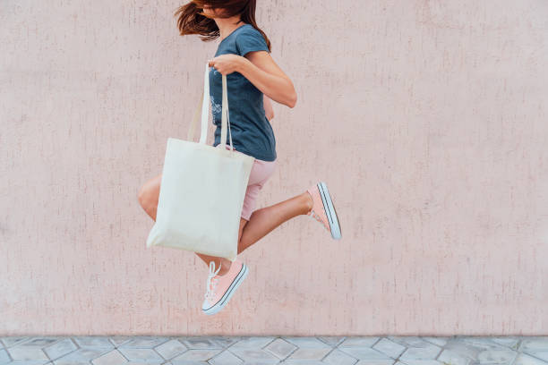 ung kvinna hoppar med vit tygkasse i händerna. - organic bag bildbanksfoton och bilder