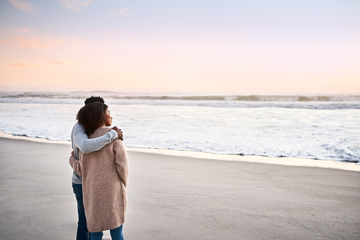 Shot of a happy young couple standing by the water’s edge and looking at the view of the ocean