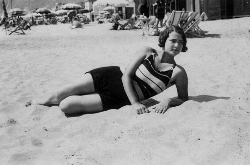 Cute young woman lying on the beach with swimsuit. 1930s black and white film. Alassio, Liguria. Italy