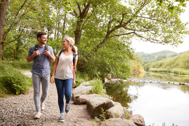 Couple Hiking Along Path By River In UK Lake District Couple Hiking Along Path By River In UK Lake District english lake district photos stock pictures, royalty-free photos & images