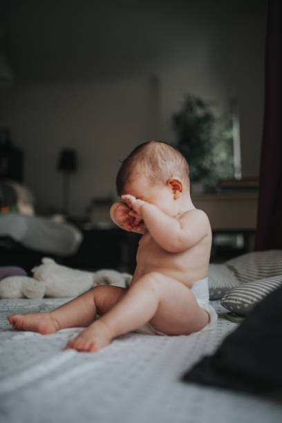 longitud completa de una niña sin camisa sentada en la cama en casa - rubbing diaper innocence babies only fotografías e imágenes de stock