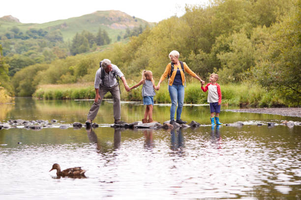 grands-parents avec leurs petits-enfants passage rivière tout en randonnée uk lake district - grandparent grandfather grandmother child photos et images de collection