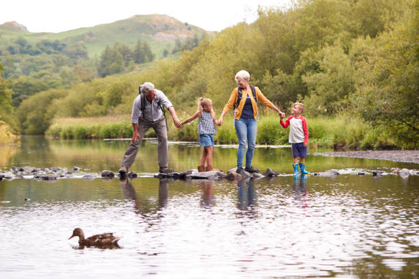 Grandparents With Grandchildren Crossing River Whilst Hiking In UK Lake District Grandparents With Grandchildren Crossing River Whilst Hiking In UK Lake District english lake district photos stock pictures, royalty-free photos & images