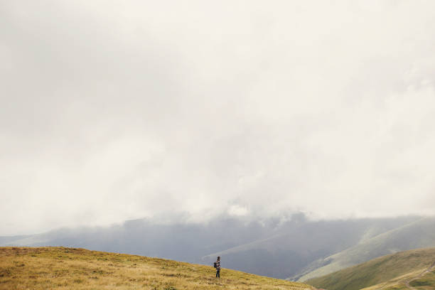 istock traveler hipster girl in hat with backpack exploring misty sunny mountains in clouds. space for text. stylish woman traveling. amazing atmospheric moment. travel and wanderlust concept. 1049857580