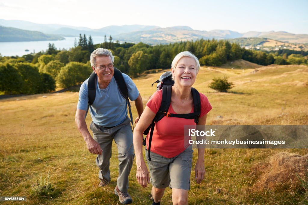 Ritratto di coppia senior che si arrampica sulla collina durante un'escursione attraverso la campagna nel Lake District UK insieme - Foto stock royalty-free di Escursionismo
