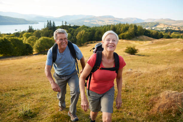 ritratto di coppia senior che si arrampica sulla collina durante un'escursione attraverso la campagna nel lake district uk insieme - hiking foto e immagini stock
