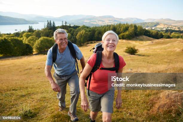 Portrait Of Senior Couple Climbing Hill On Hike Through Countryside In Lake District Uk Together Stock Photo - Download Image Now