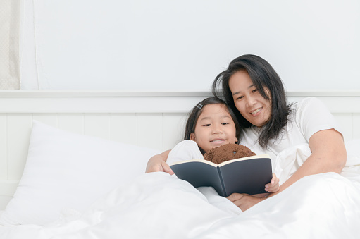 Mother read book with daughter together on bed, education concept