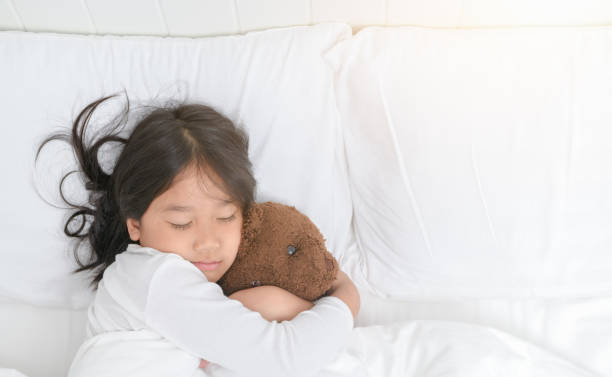 istock Girl is hugging teddy bear while sleeping in bed 1049862940