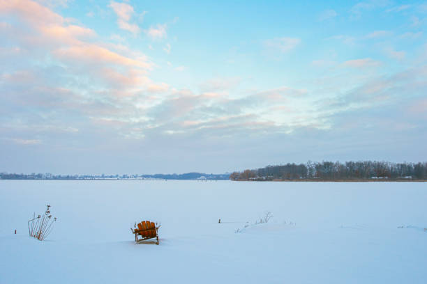 This is an adirondack chair sitting by a lake. The chair was put in this position and photographed for months sitting in the same position. I moved it only to mow around it. The chair deteriorated over time and the process of ending the project was accelerated because people instead upon sitting in / on this broken chair.This image is in winter with lots of snow around the chair.