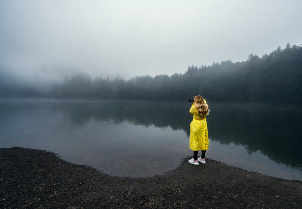 Rear View Of Woman Photographing On Field Against A Dark Lake