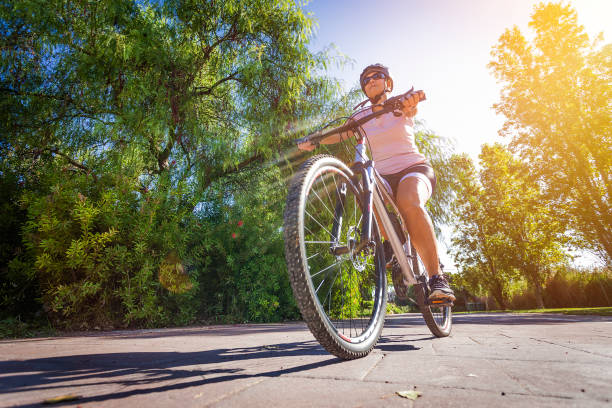 Low angle view of a mature woman cycling on a mountain bike in an urban park. The woman is wearing sport clothes Predominant color is green. Copy space available for text and/or logo. DSRL outdoors photo taken with Canon EOS 5D Mk II and Canon EF 17-40mm f/4L IS USM Wide Angle Zoom Lens