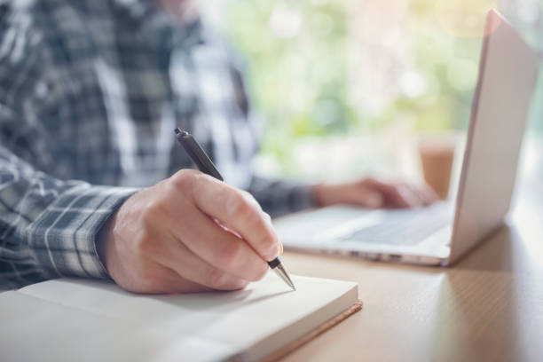 Businessman writing at desk in office with laptop computer