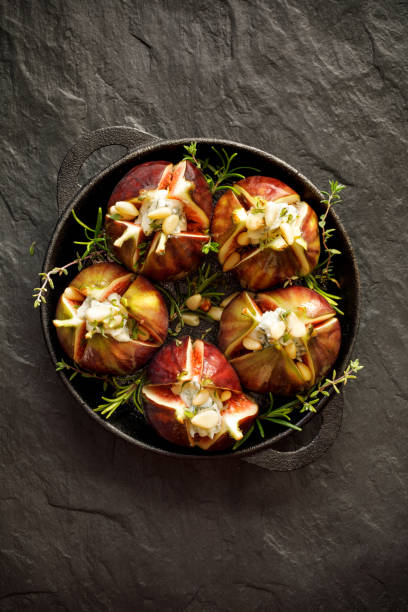 Fresh figs stuffed with gorgonzola cheese, pine nuts, honey and herbs in a black dish on a dark, stone background, top view. Fresh figs stuffed with gorgonzola cheese, pine nuts, honey and herbs in a black dish on a dark, stone background, top view. Excellent, tasty, vegetarian snack, appetizer plate fig blue cheese cheese stock pictures, royalty-free photos & images