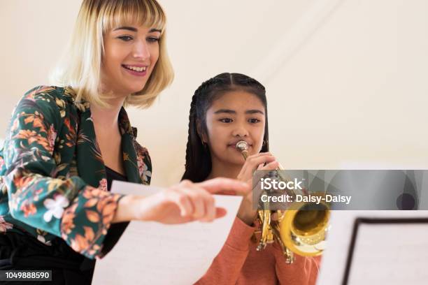 Teacher Helping Female Student To Play Trumpet In Music Lesson Stock Photo - Download Image Now