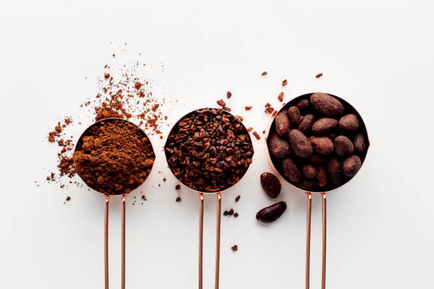 Cocoa Rose gold measuring cups of cocoa beans, cacao nips and cocoa powder on a white background, flat lay healthy food concept cacao nib stock pictures, royalty-free photos & images