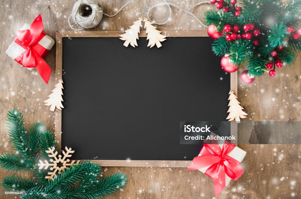 Empty blackboard with christmas decoration, red gift box, fir branches. Empty blackboard with christmas decoration, red gift box, fir branches. Chalk board and Christmas trinkets. Xmas background with copy space for inscription, top view. Snow effect. Christmas Stock Photo